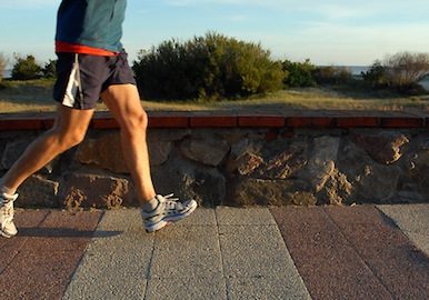 Young male athlete jogging at the promenade. Legs in motion. A quiet beach with sand dunes on the background